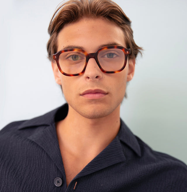 Model with short brown hair in a black linen shirt wearing Bogota Optical Havana Optical