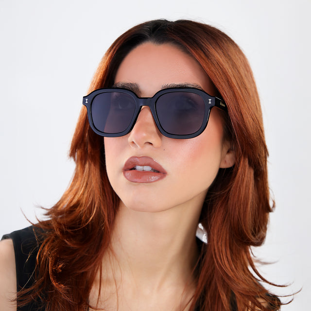 Another angle of woman with red hair in a black blouse, looking right wearing Bogota E Sunglasses Black with Grey Flat