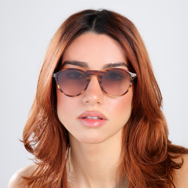 Woman with red hair in an olive blouse wearing Capri Sunglasses Sand Dune with Brown Gradient
