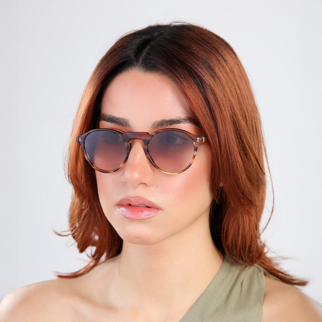 Woman with red hair in an olive blouse, looking right wearing Capri Sunglasses Sand Dune with Brown Gradient