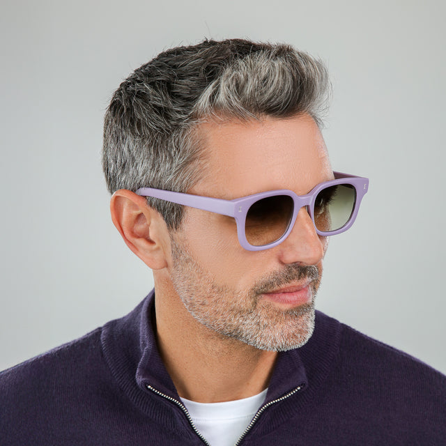Model with salt and pepper hair and beard in a dark plum half-zip looking left wearing Ellison Sunglasses Matte Lavender with Olive Flat Gradient