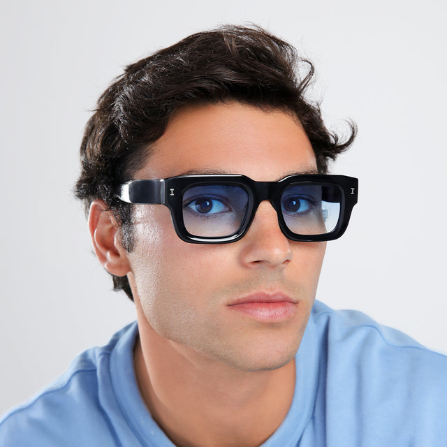 Man in a baby blue shirt turning to the left while looking right wearing Lewis 50 Sunglasses Black with Blue Flat Gradient See Through