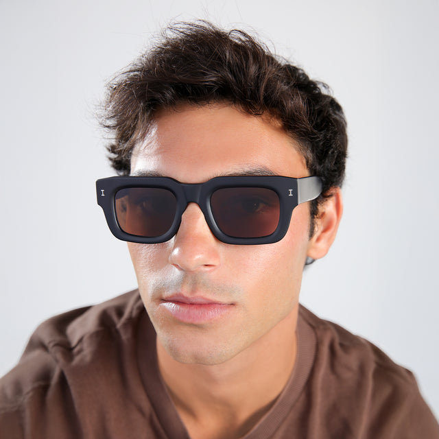 Man with brown hair in a brown shirt wearing Lewis 50 Sunglasses Matte Black with Brown Flat