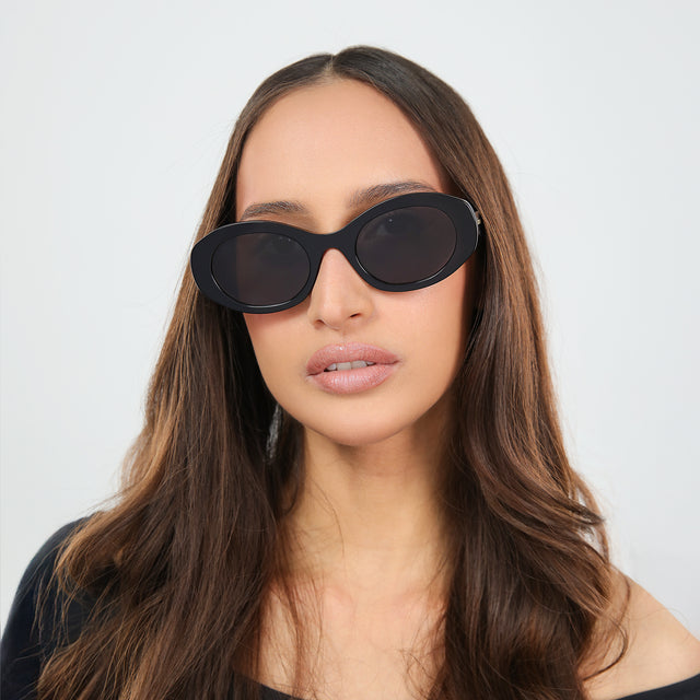 Brunette woman in an off-the-shoulder blouse wearing Luna Sunglasses Black with Grey Flat