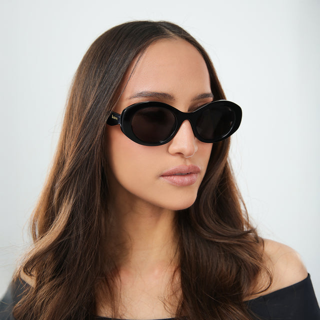 Brunette woman in an off-the-shoulder blouse looking to her left wearing Luna Sunglasses Black with Grey Flat