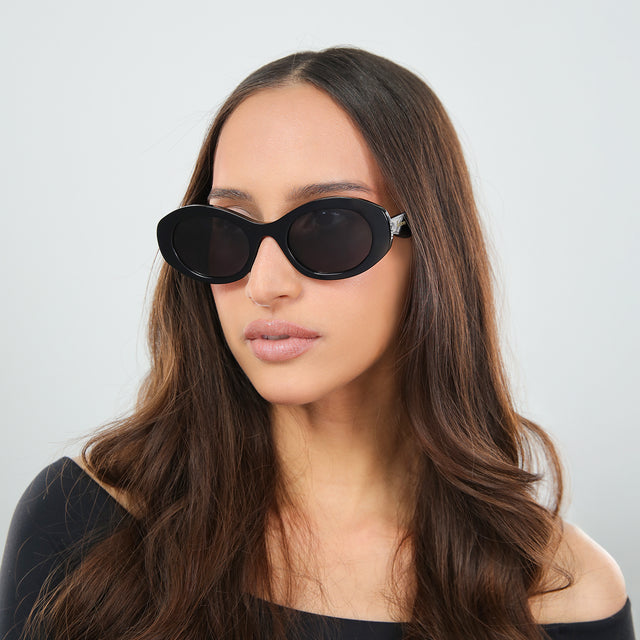 Another angle of brunette woman in an off-the-shoulder blouse wearing Luna Sunglasses Black with Grey Flat