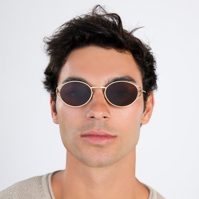 Man with brown hair in a beige waffled sweatshirt wearing Maria Sunglasses Gold with Brown