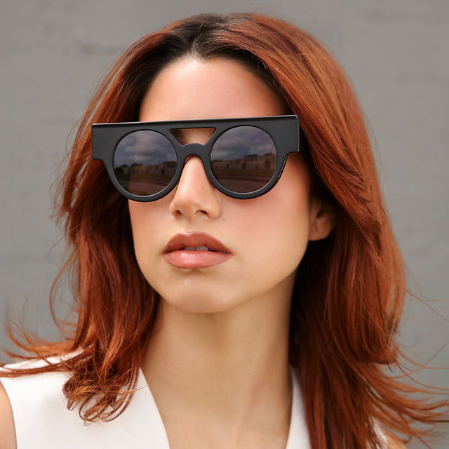 Model with red hair near a brick wall wearing Meyer (15 Year Anniversary) Sunglasses Matte Black with Grey Flat