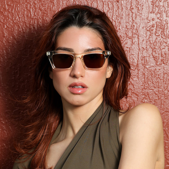 Woman near a maroon wall wearing Portugal Sunglasses Champagne with Brown Flat