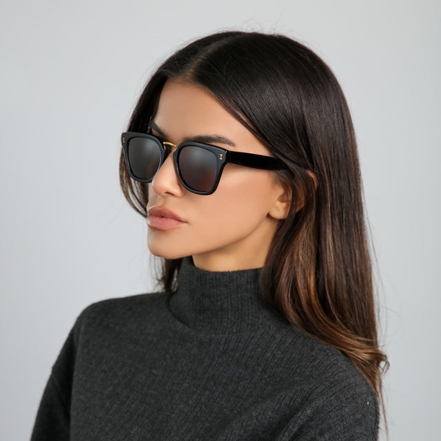 Another angle of brunette woman in a gray turtleneck wearing Positano Sunglasses Black/Gold with Grey