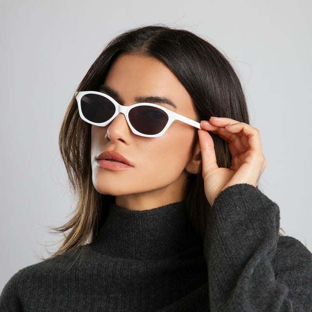 Angled portrait image of brunette woman in a black cashmere turtleneck wearing Vilma Sunglasses Light Grey with Grey