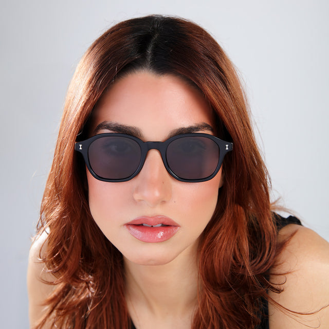 Close up of woman with red hair in a black blouse wearing William Sunglasses Black with Grey