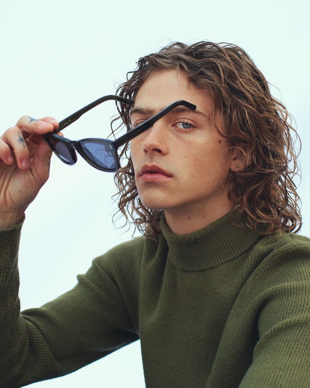 Model with medium wavy hair in a dark green turtleneck wearing Austin Sunglasses Black with Grey Flat