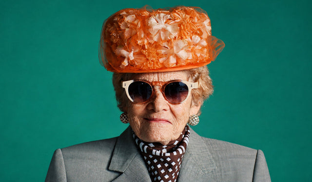 Woman in a large, coral tea hat wearing the Leonard Sunglasses in the limited edition Anniversary color
