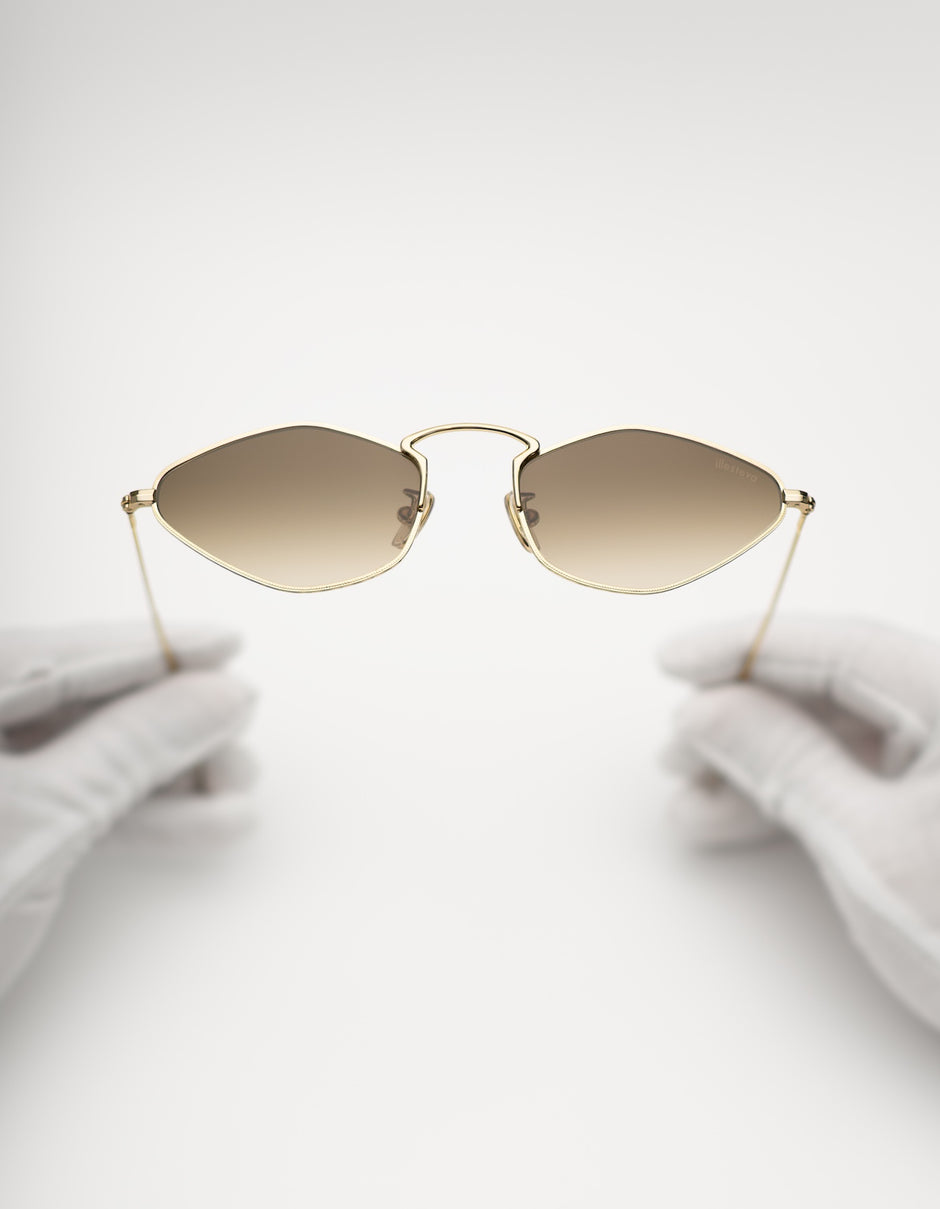 Astoria sunglasses in Gold with Taupe gradient lenses, held by gloved hands