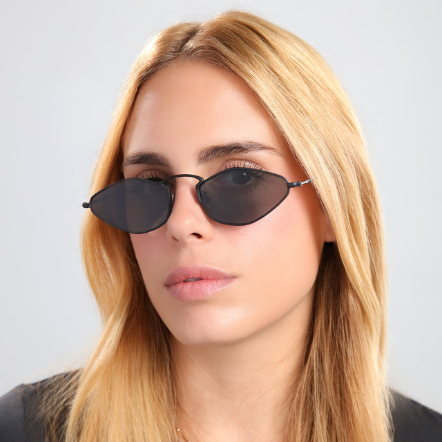 Blond woman in a black tee wearing Austria Sunglasses Matte Black with Grey Flat