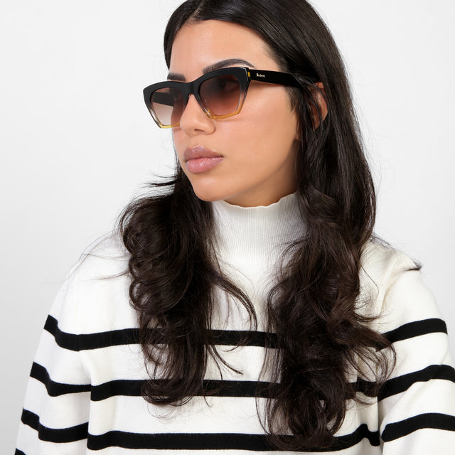 Brunette model in a black and white striped turtleneck looking right wearing Bali Sunglasses Horizon Black with Brown Gradient