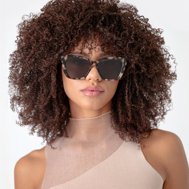 Brunette model with afro-curly hair wearing Barcelona Sunglasses White Tortoise with Grey Flat