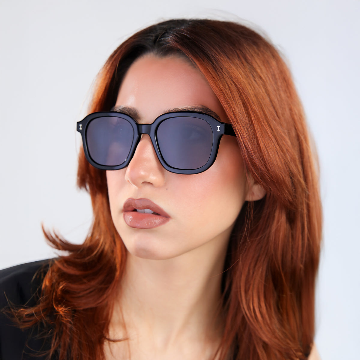 Woman wearing Bogota E Sunglasses in Black with Grey Flat lenses, side profile, Woman with red hair in a black blouse, looking right
