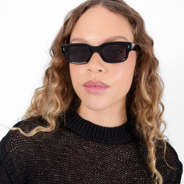 Brunette model with ombré, natural curls wearing Cali Sunglasses Black with Grey