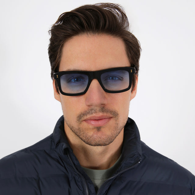 Model with short brown hair in a navy puffer coat wearing Catania Sunglasses Black/Gold with Blue Flat Gradient See Through