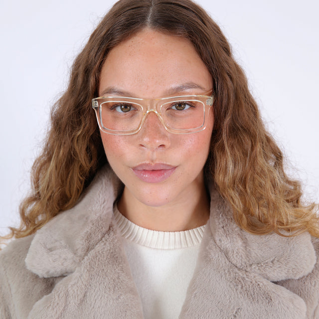 Brunette model with wavy ombre hair in a beige fuzzy jacket wearing Catania Optical Champagne Optical