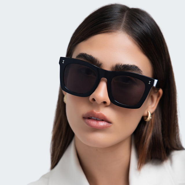 Brunette model in a beige blazer wearing Charleston Sunglasses Black with Grey Flat