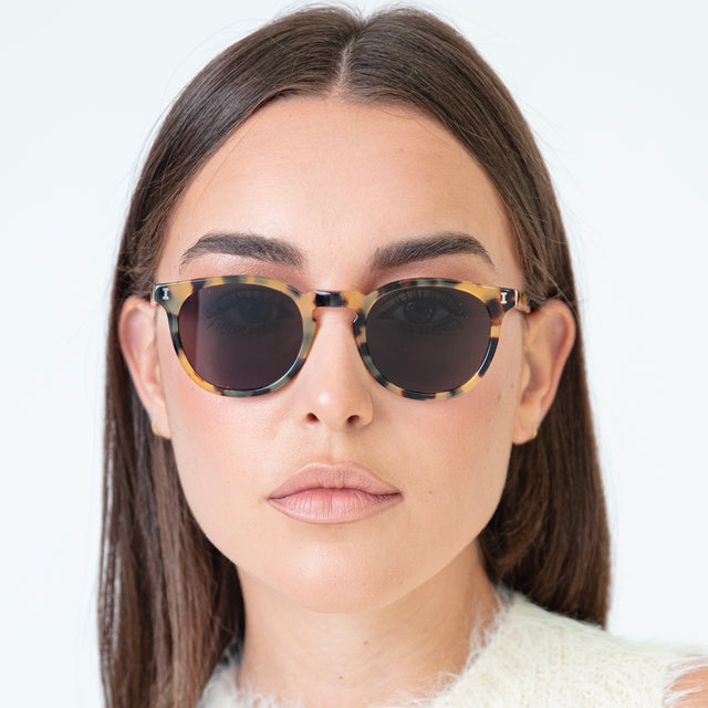 Brunette model in a fuzzy, sweater vest wearing Eldridge 48 Sunglasses Tortoise with Grey Flat