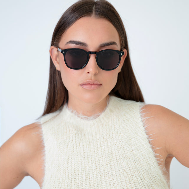 Brunette model in a fuzzy sweater vest wearing Eldridge Sunglasses Black with Grey Flat