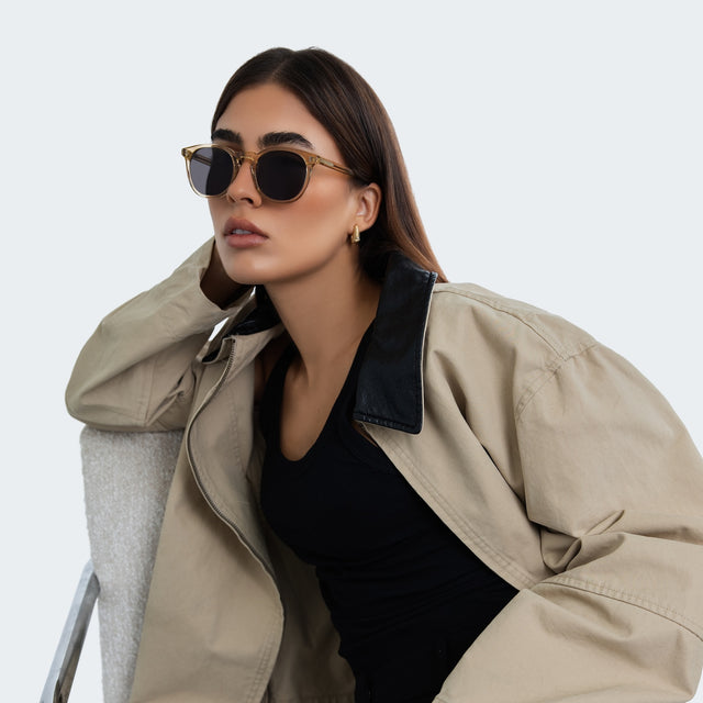 Woman in a trench coat leaning on studio chair wearing Eldridge 56 Sunglasses Citrine with Grey Flat