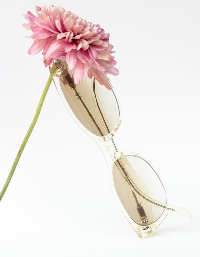 Encinitas sunglasses in Champagne leaning against a pink flower on a white background