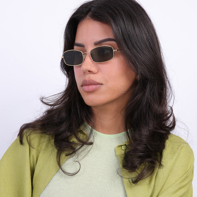 Brunette model with loose curls looking right wearing Flushing Sunglasses Gold with Olive Flat