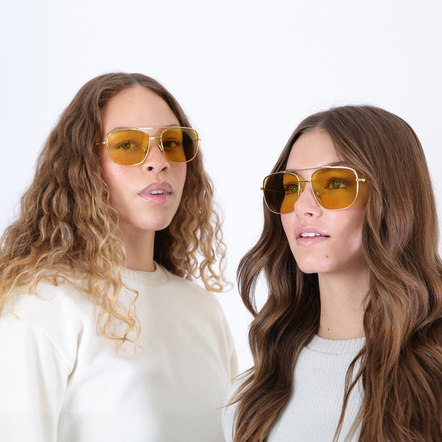 Two models with wavy hair wearing Frankie Sunglasses Gold with Honey Flat See Through