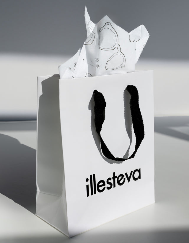 White shopping bag with 'illesteva' logo and sunglasses packaging on a gray background