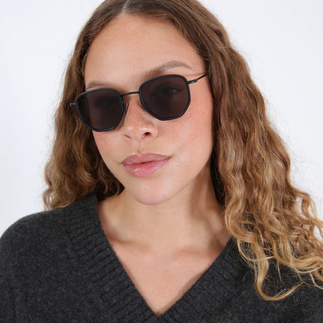 Brunette model in a wool v-neck sweater wearing Hunter Ace Sunglasses Matte Black with Grey