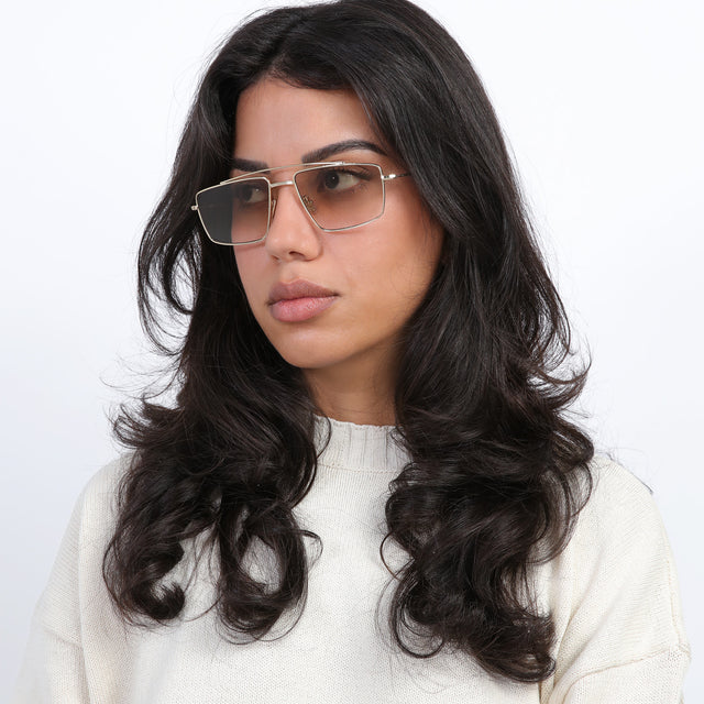 Brunette model with loose curls looking right wearing Jane Sunglasses Gold with Taupe Gradient