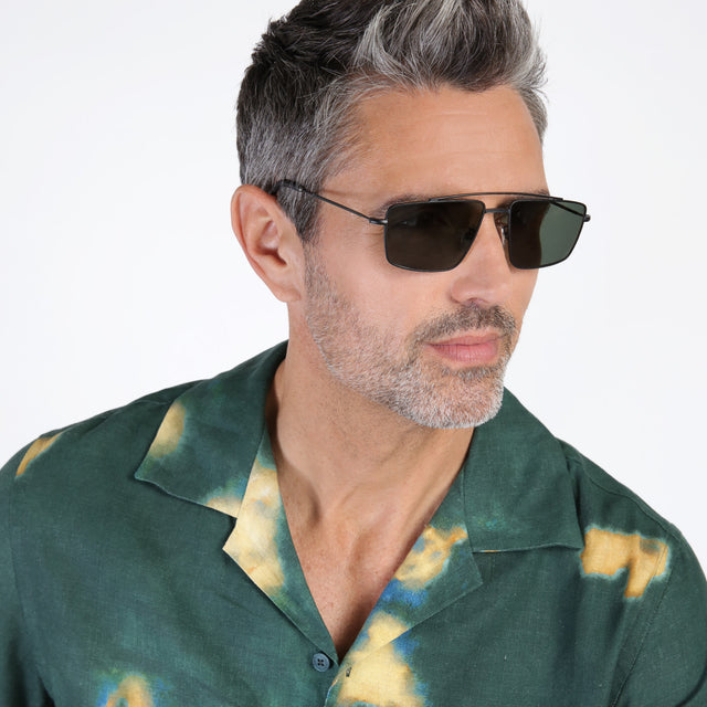 Model with salt and pepper beard looking left wearing Jane Sunglasses Matte Black with Olive