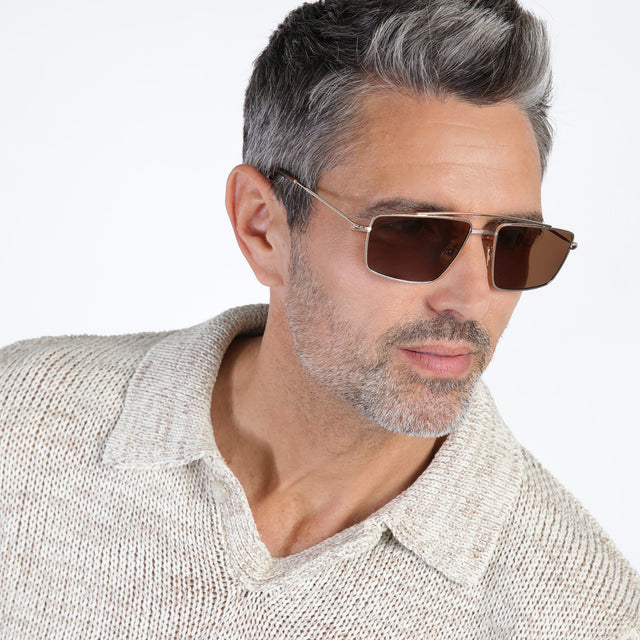 Model with salt and pepper beard looking left wearing Jane Sunglasses Rose Gold with Brown