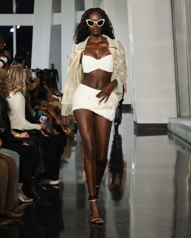 Model walking on a runway wearing a white outfit with Kim Shui x illesteva in cream