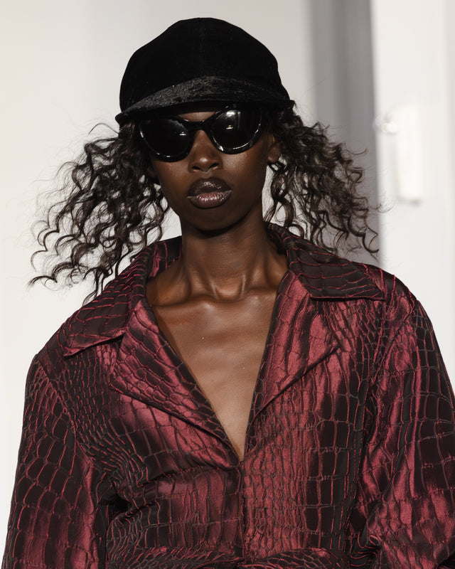 Person wearing a black cap and Kim Shui x illesteva sunglasses with a textured red garment.
