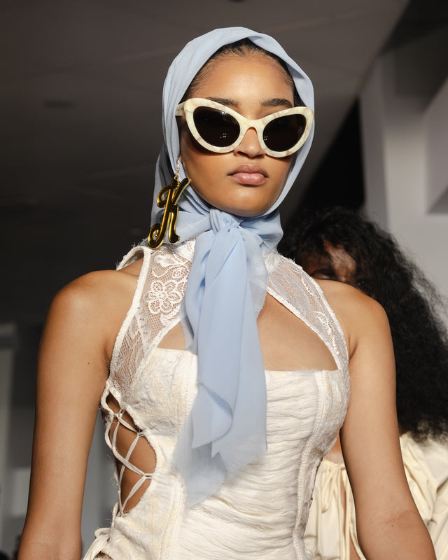 Model wearing a white dress with a cut-out design, Kim Shui x illesteva sunglasses, and a light blue headscarf.