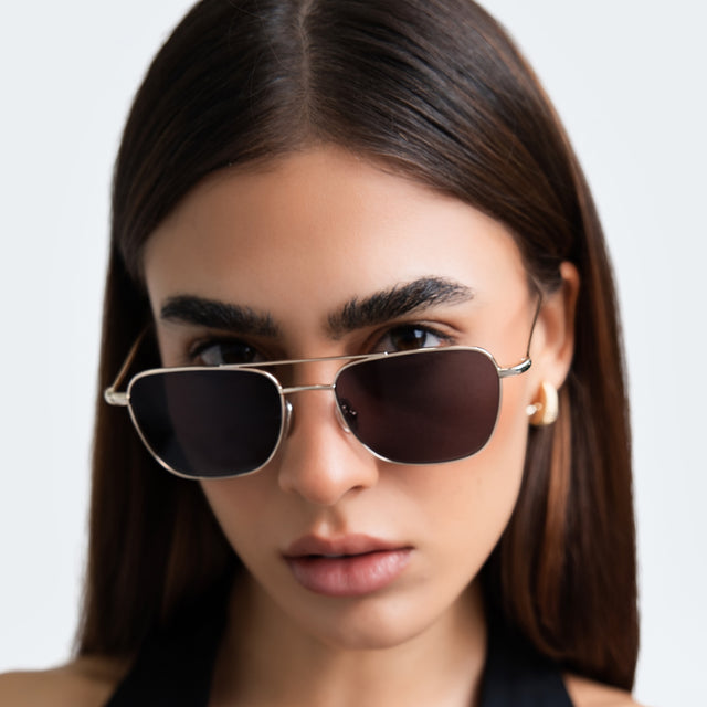 Another angle of woman with gold hoop earrings in a black blouse wearing Lafayette Sunglasses Gold with Grey Flat