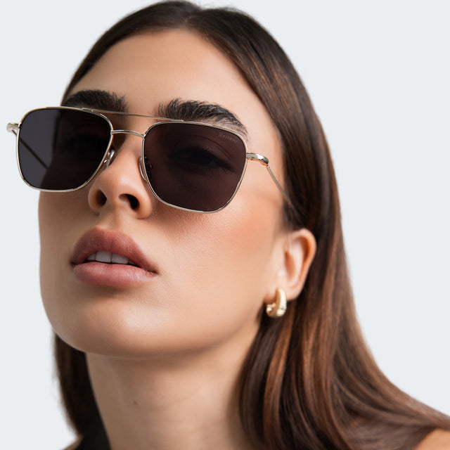 Woman with gold hoop earrings wearing Lafayette Sunglasses Gold with Grey Flat