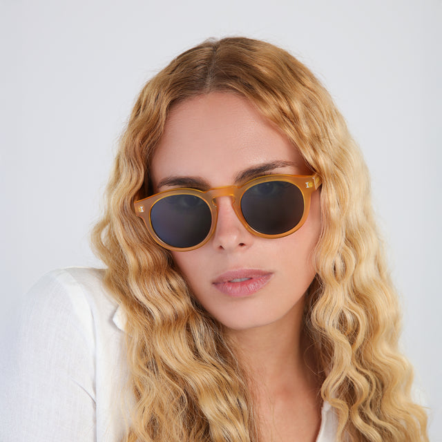 Woman with wavy, blond hair in a linen blouse wearing Leonard (15 Year Anniversary) Sunglasses Honey Gold with Olive