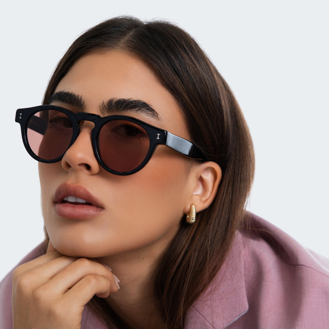 Woman in a pink blazer wearing Leonard Sunglasses Black with Plum See Through