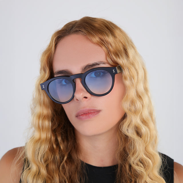 Blond woman with wavy hair in a black blouse wearing Leonard Sunglasses Black with Blue Gradient See Through