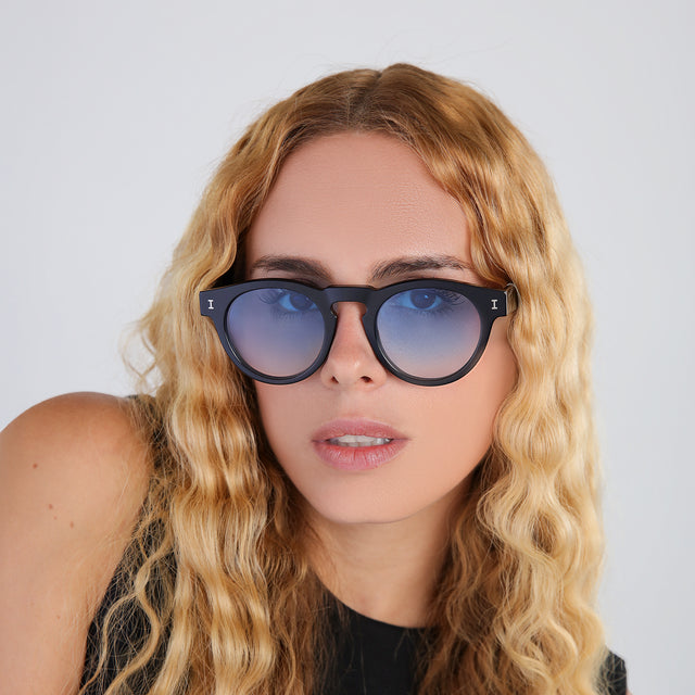 Another angle of blond woman with wavy hair in a black blouse wearing Leonard Sunglasses Black with Blue Gradient See Through