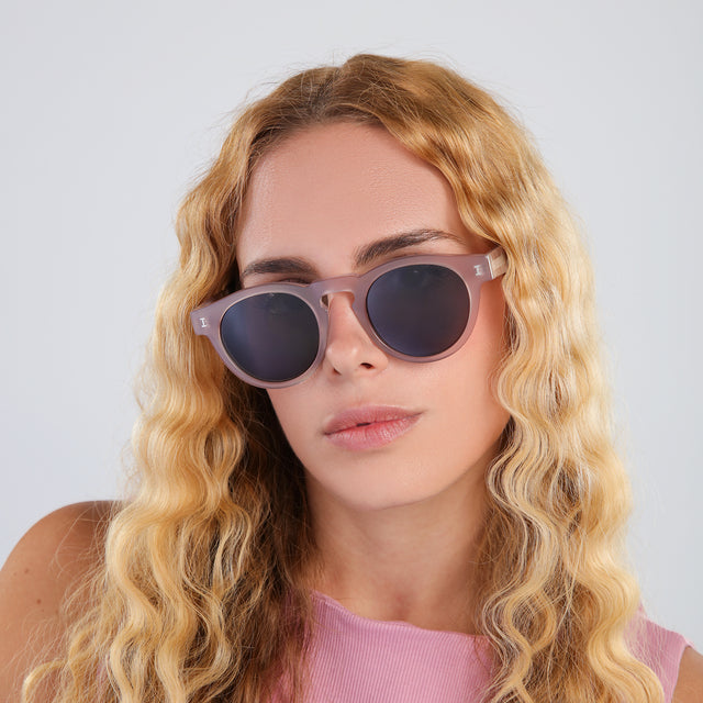Blond woman with wavy hair in a pink blouse wearing Leonard Sunglasses Thistle with Grey