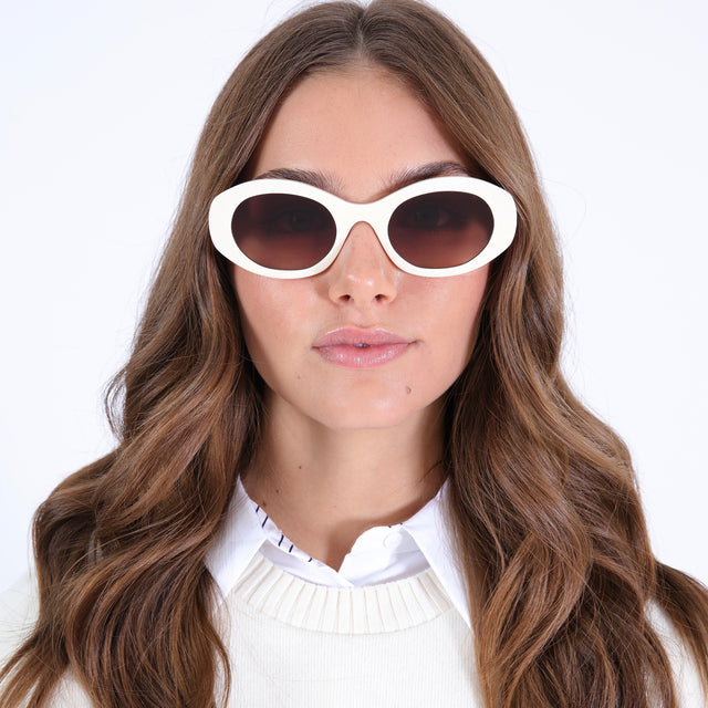 Brunette model in a white collared blouse with a sweater vest wearing Luna Sunglasses Cream with Brown Flat Gradient