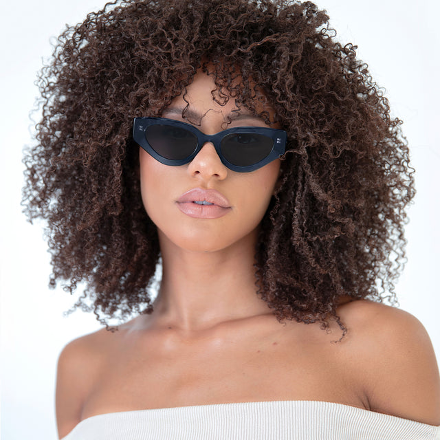 Brunette model with natural curls wearing Mary Lou Sunglasses Navy with Grey Flat